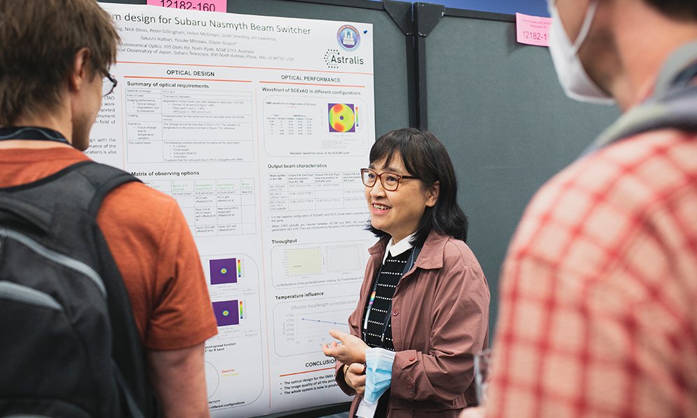 Presenter speaking with attendees beside a scientific research poster display at a conference or academic poster session.