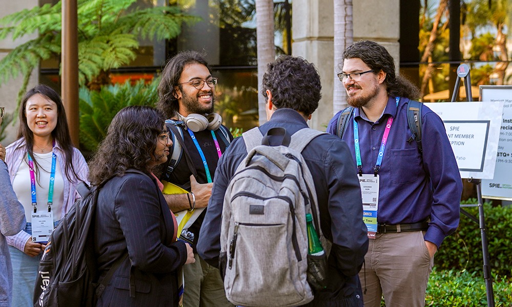 Group of conference attendees wearing event badges and backpacks talking together outdoors between sessions.